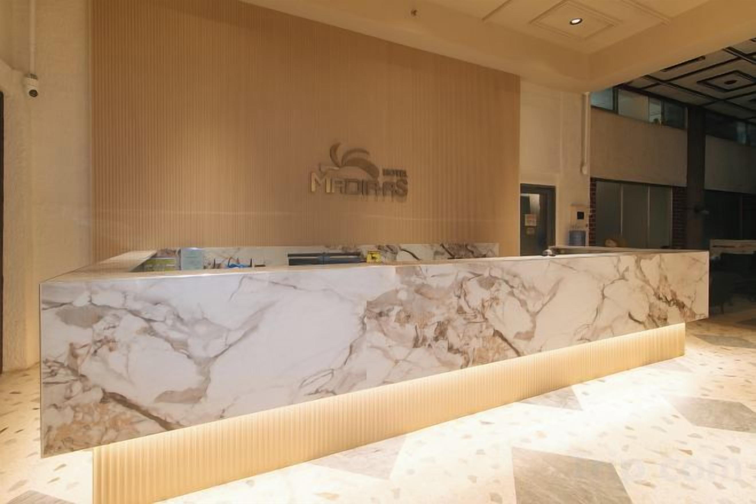 A reception desk with a marble top, a wooden wall with a logo, and a modern interior design.