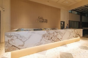 Un comptoir d’accueil avec un plateau en marbre, un mur en bois orné d’un logo et un aménagement intérieur moderne.