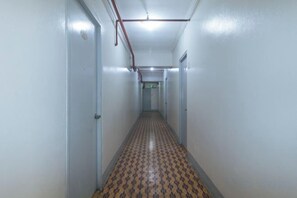 Un pasillo estrecho con puertas a ambos lados, un suelo estampado y tuberías en el techo.
