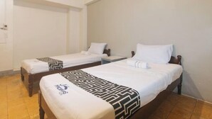 A room with two single beds, wooden headboards, white bedding, and a patterned throw on the bed in the foreground.