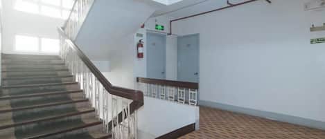 A staircase with a handrail leading to an upper floor, a fire alarm on the wall, and a patterned carpet.