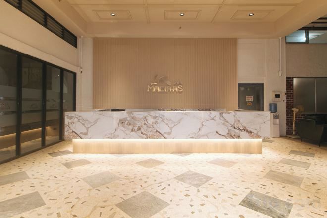 A reception area with a marble counter, a wooden wall with the hotel name, and a tiled floor.