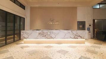 A reception area with a marble counter, a wooden wall with the hotel name, and a tiled floor.
