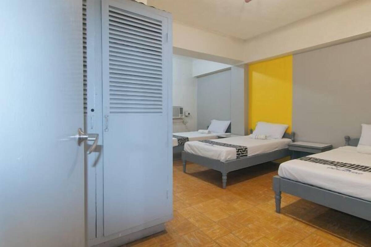 Una habitación de hotel con dos camas, un armario y un baño visible al fondo.