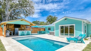 Un jardin avec une piscine, un espace barbecue et une terrasse couverte.