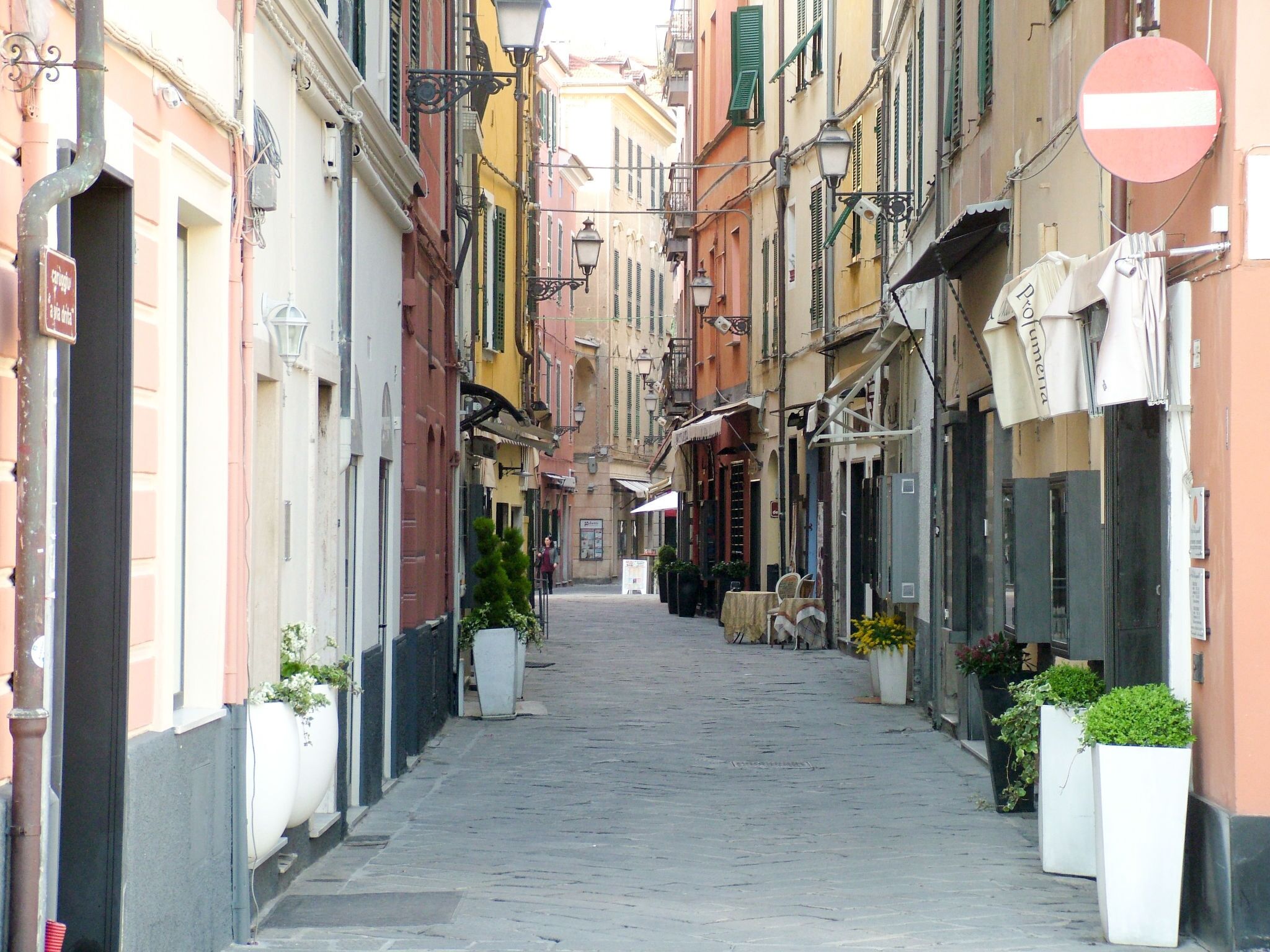 A narrow cobblestone street lined with colorful buildings, a no entry sign, and outdoor seating areas.