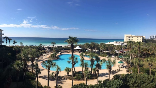 A resort with a large pool surrounded by palm trees and a view of the ocean. - The Crescent 210 (Miramar Beach)