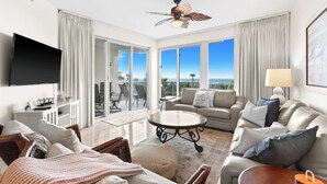 A spacious living room with a large flat-screen TV, comfortable seating, a ceiling fan, and a balcony with a view of the ocean. - The Crescent 210 (Miramar Beach)