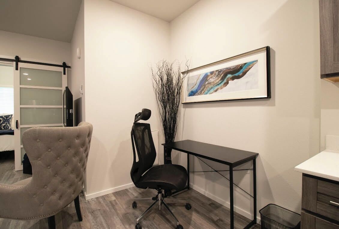 A modern office space with a tufted office chair, a black office chair, a desk, and a framed abstract painting on the wall.