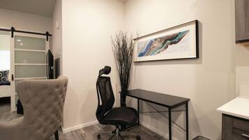 A modern office space with a tufted office chair, a black office chair, a desk, and a framed abstract painting on the wall.