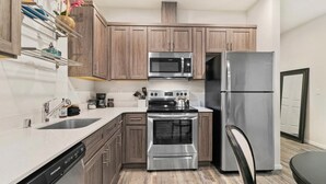 Una cocina compacta con armarios de madera, un refrigerador de acero inoxidable, un microondas, un horno y un lavavajillas.