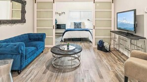 Una sala de estar moderna con un sofá azul, una mesa de centro redonda, un sillón beige y un televisor. La habitación cuenta con un armario corredero, un espejo montado en la pared y un televisor de pared. Los servicios incluyen estacionamiento gratuito, lavadora/secadora, aire acondicionado y un ambiente tranquilo.