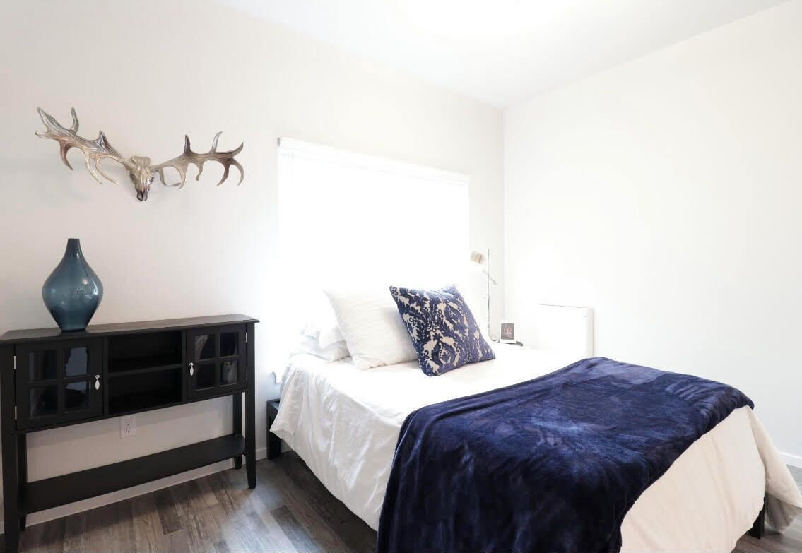 A bedroom with a bed, a nightstand, a dresser, and a wall-mounted deer head decoration.