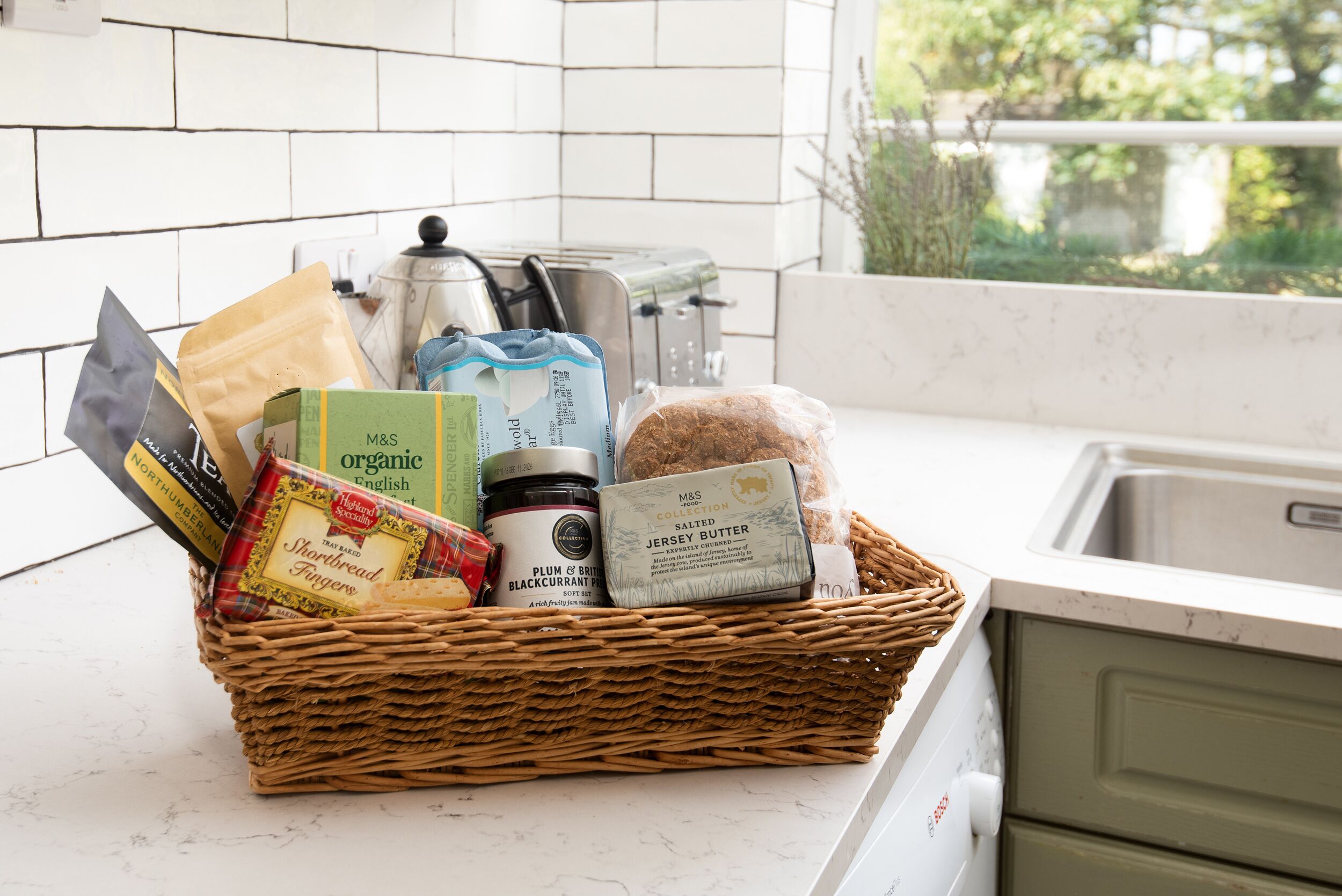 A kitchen counter with a wicker basket containing various food items and kitchen appliances.