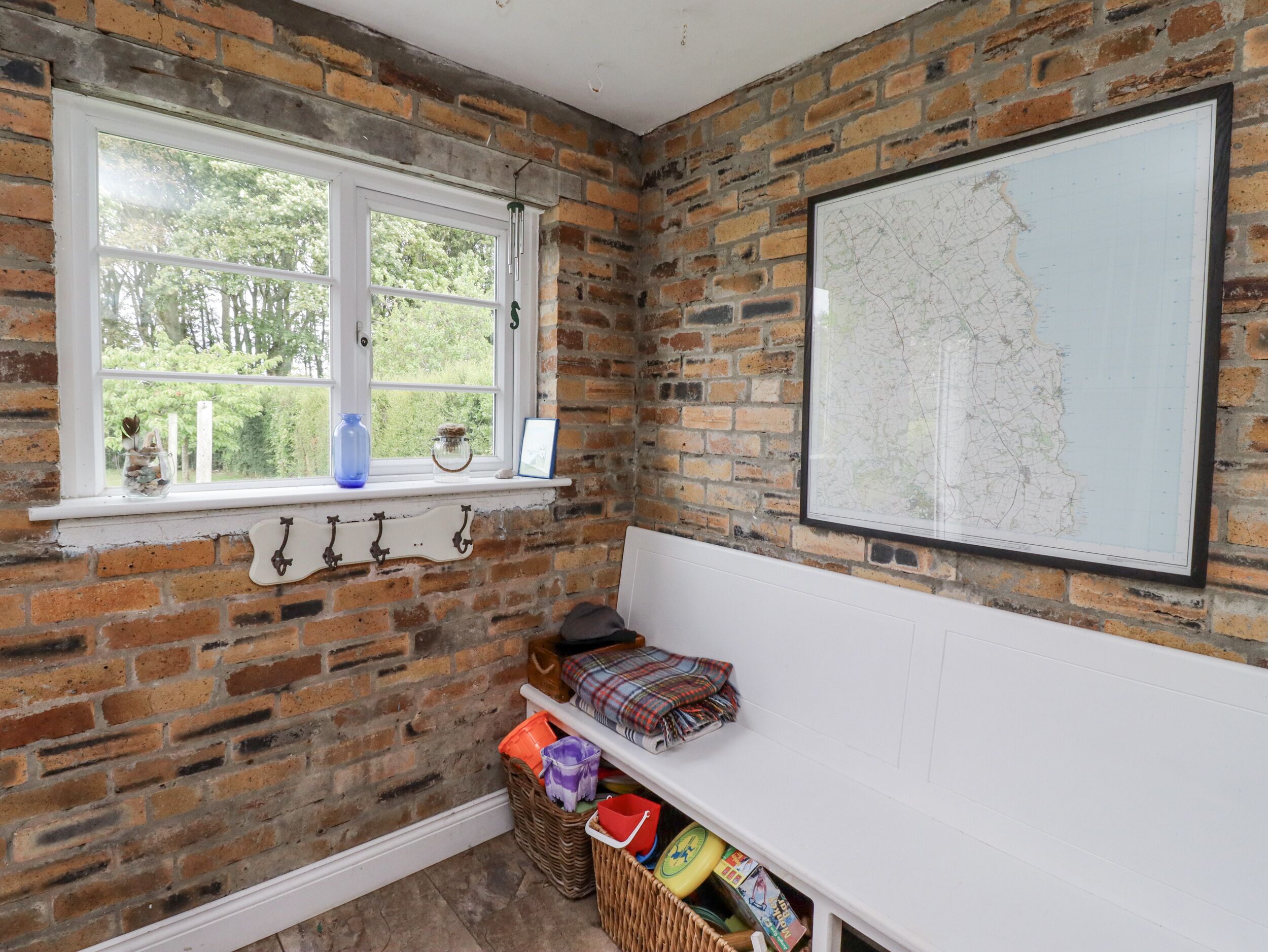 Une pièce avec un mur en briques, une fenêtre donnant sur un paysage verdoyant, une carte accrochée au mur et une étagère contenant divers objets.