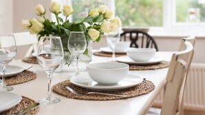A dining table set with white plates, bowls, and wine glasses, with a vase of white roses in the center. - Driftwood (Alnwick)