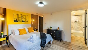 A modern bedroom with a bed, bedside tables, a dresser, and a bathroom with a bathtub.
