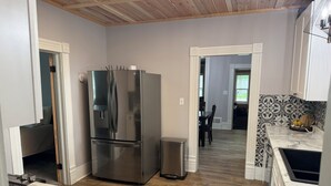 A modern kitchen with a stainless steel refrigerator, wooden flooring, and a marble countertop.