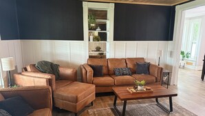 A living room with a brown leather sofa, a matching armchair, a coffee table, and a bookshelf.