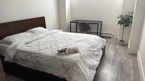 A bedroom with a bed, a desk, a chair, and a potted plant.
