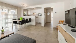 Une cuisine moderne avec des meubles blancs, un coin repas comprenant une table et des chaises, et un téléviseur posé sur un meuble en bois.