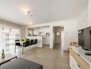 A modern kitchen with white cabinets, a dining area with a table and chairs, and a TV on a wooden stand.
