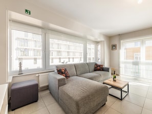 A modern living room with a grey sectional sofa, a small table with a bottle, and a bench.