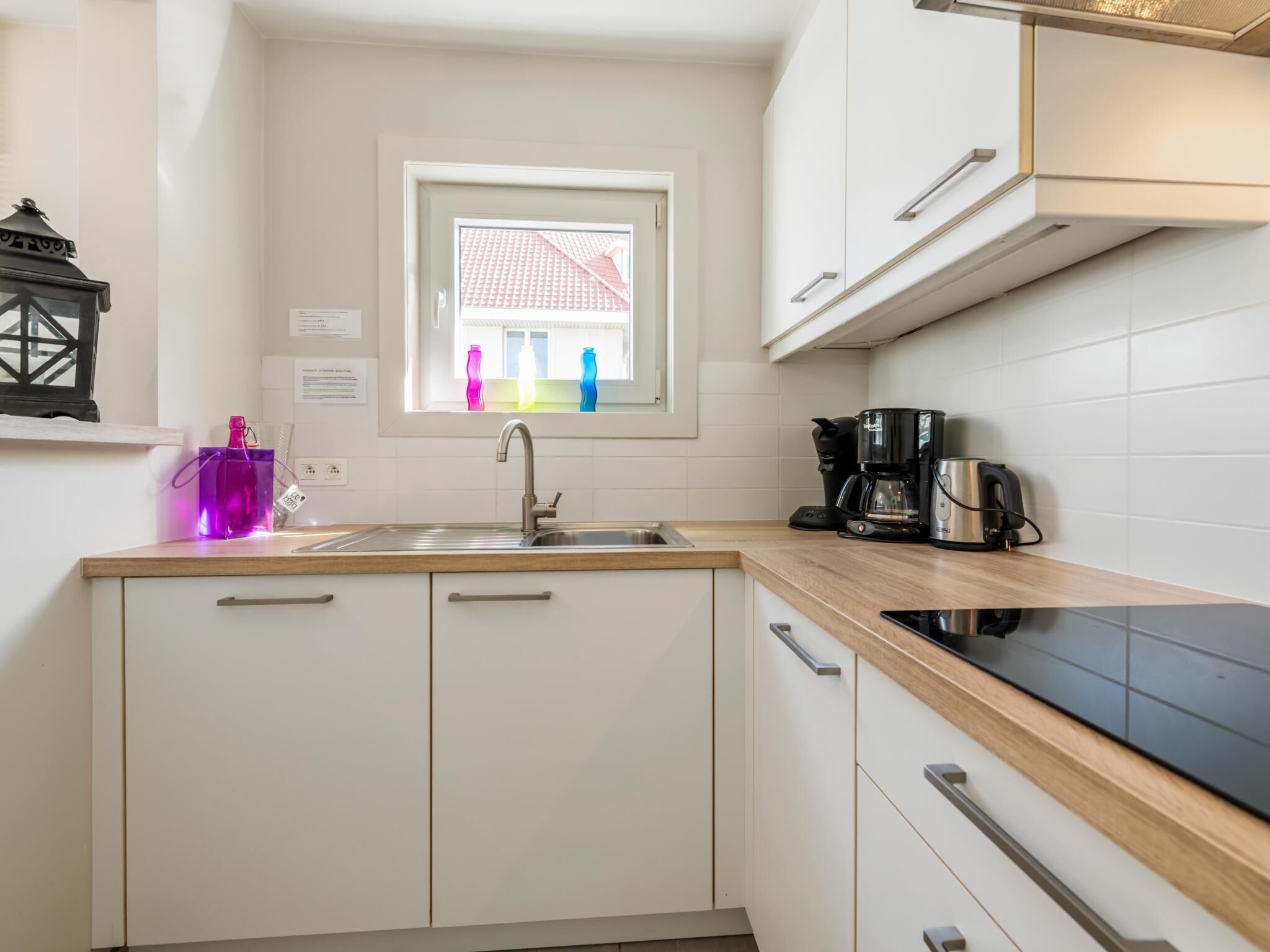 A modern kitchen with white cabinets, a black countertop, a stainless steel sink, and a window with a view of colorful buildings.