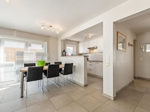 A modern kitchen with white cabinets, a dining area with a wooden table and black chairs, and a window with blinds.