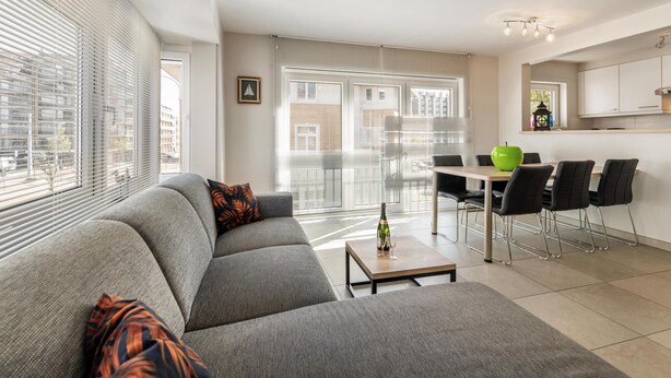 Un salon moderne comprenant un canapé, une table à manger avec des chaises et un coin cuisine avec des placards.