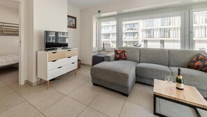 Un salon moderne avec un canapé, un téléviseur et une bouteille de champagne posée sur une table.