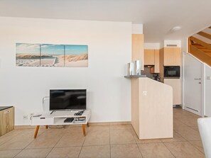 A modern living room with a flat-screen TV, a coffee table, and a bookshelf.