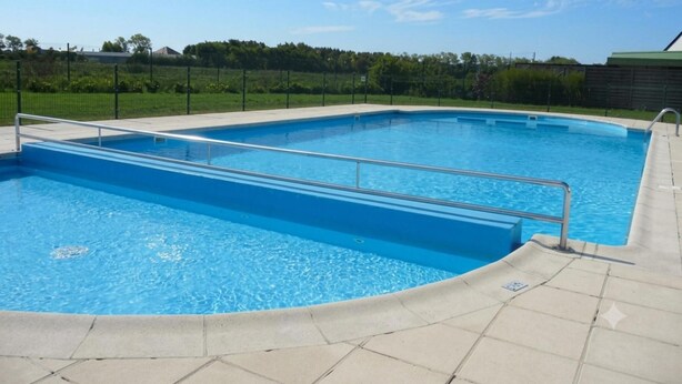 Piscina rectangular con barandilla de seguridad metálica, rodeada por un solárium con baldosas.