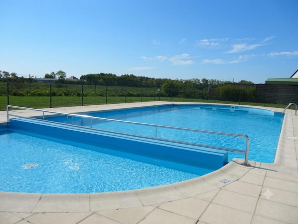 A rectangular swimming pool with a metal safety railing, surrounded by a tiled deck.