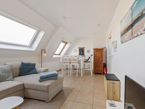 A modern living room with a sectional sofa, a dining table with chairs, a fireplace, and a view of the sky through skylights.
