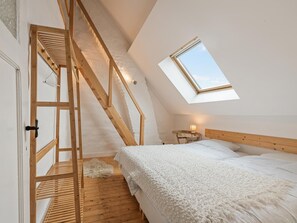 A bedroom with a sloped ceiling, a skylight, a wooden staircase, a bed with white bedding, and a small bedside table with a lamp. - Spacious town house in the centre of Nieuwpoort (Nieuwpoort)