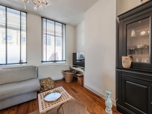 Una sala de estar con un sofá gris, una mesita con una bandeja, un televisor sobre un mueble bajo y un aparador de madera oscura con puertas de vidrio.