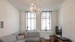 Un salon moderne avec un canapé gris, une table basse en bois, un téléviseur posé sur un meuble et un lustre.