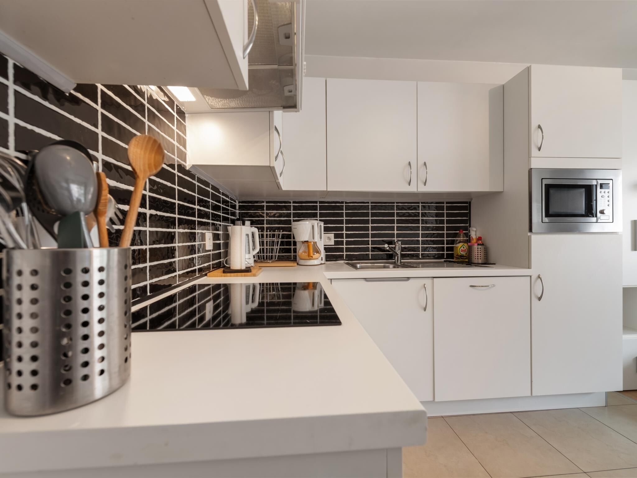 A modern kitchen with white cabinets, a black and white backsplash, a stainless steel sink, and a microwave.