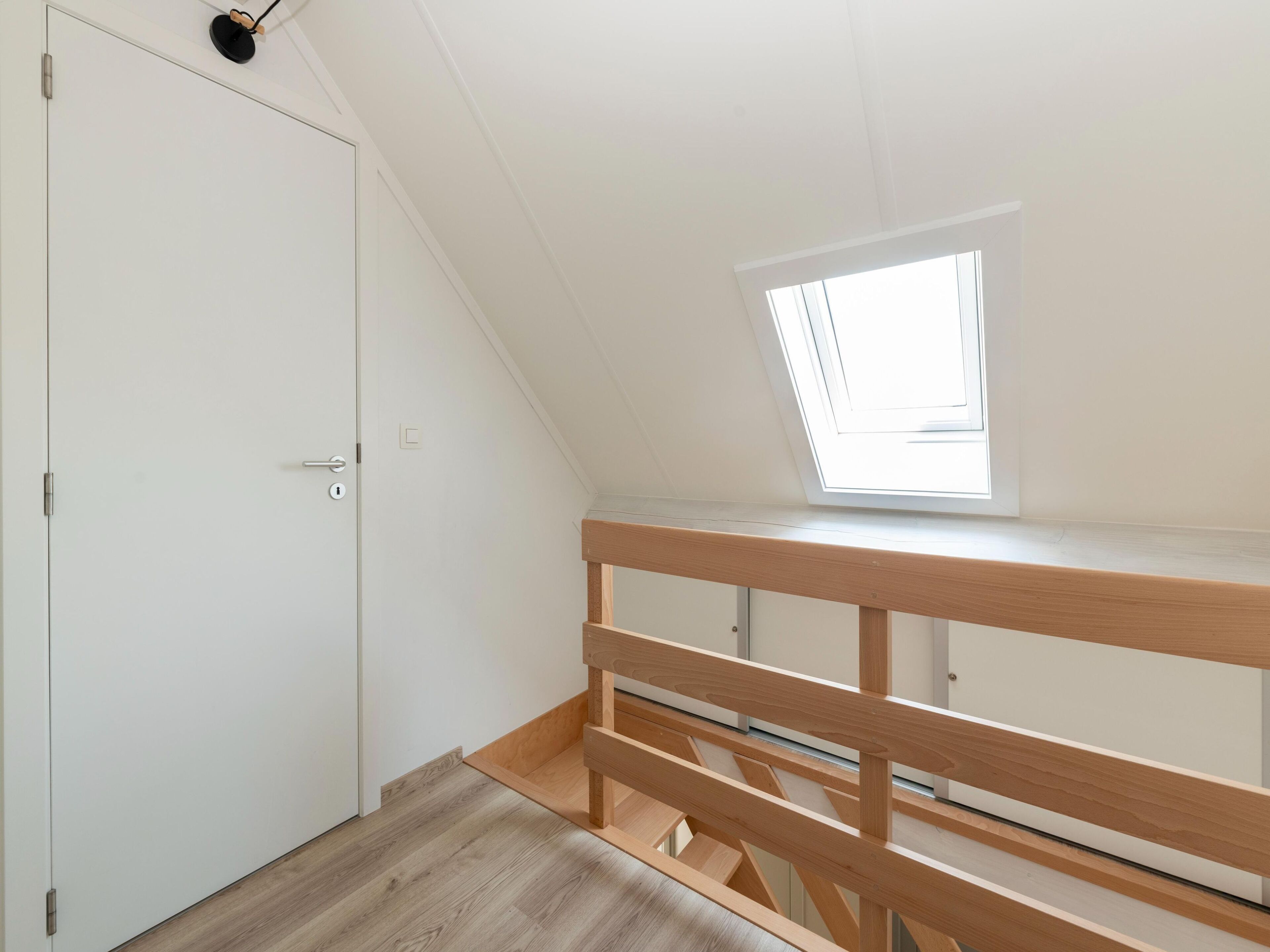 Una habitación con techo inclinado, tragaluces, un banco de madera y una puerta blanca.