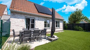 Een huis met pannendak, bakstenen gevel en een terras met tafel en stoelen.