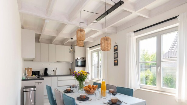 Een moderne keuken met witte kasten, een eettafel compleet met blauwe stoelen, en een ontbijt met croissants en sinaasappelsap.