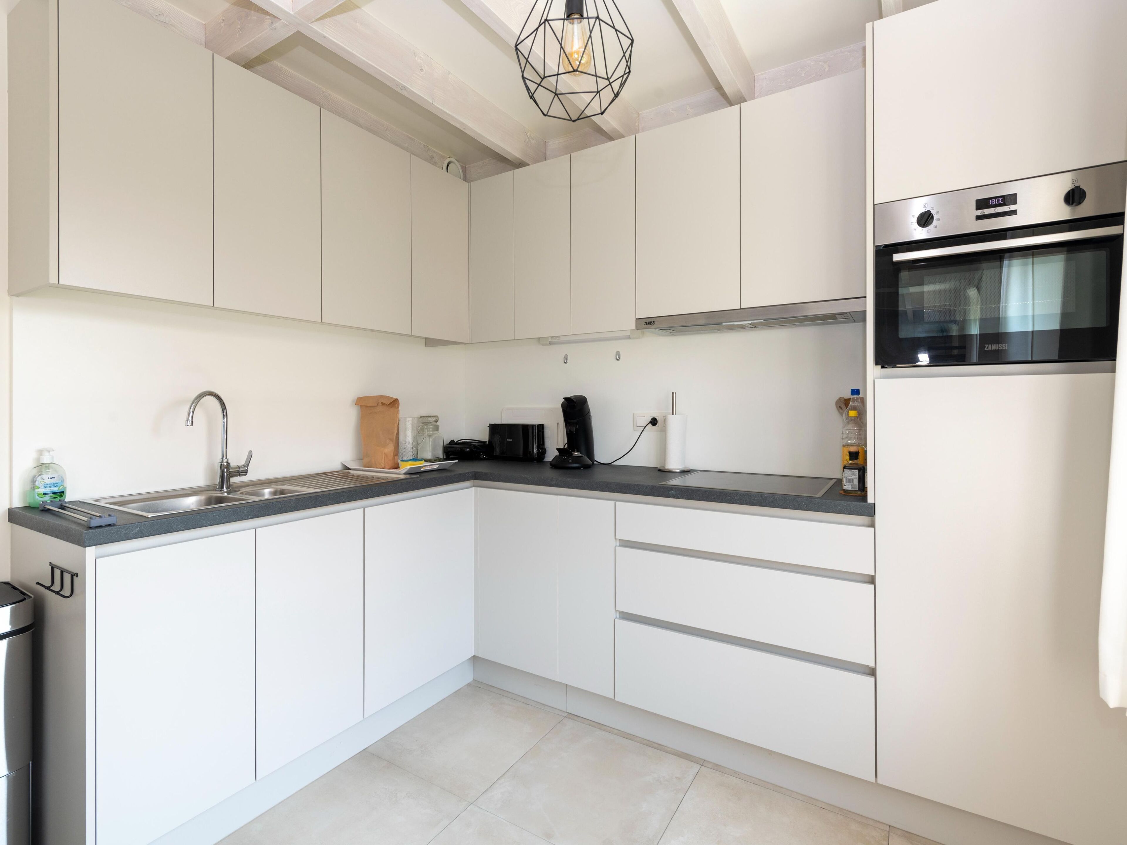 A modern kitchen with white cabinets, a stainless steel sink, a built-in oven, and a coffee maker.