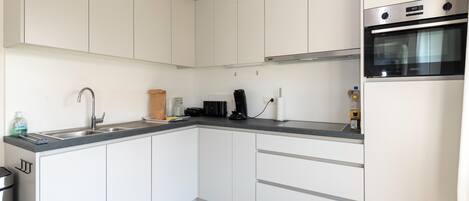 A modern kitchen with white cabinets, a stainless steel sink, a built-in oven, and a coffee maker.