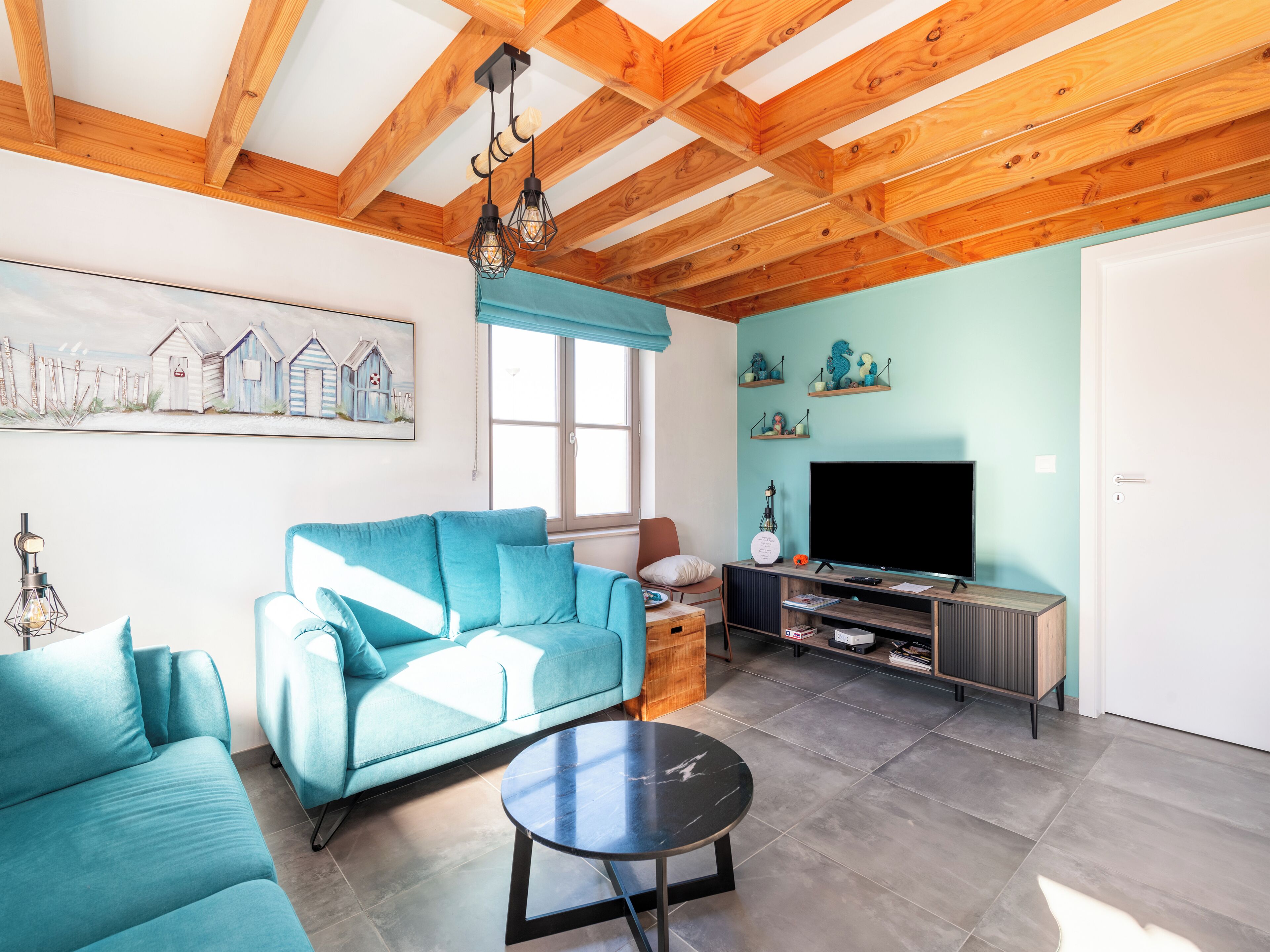 Een woonkamer met een blauwgroene bank, een zwarte salontafel, een televisie en houten balken in het plafond.