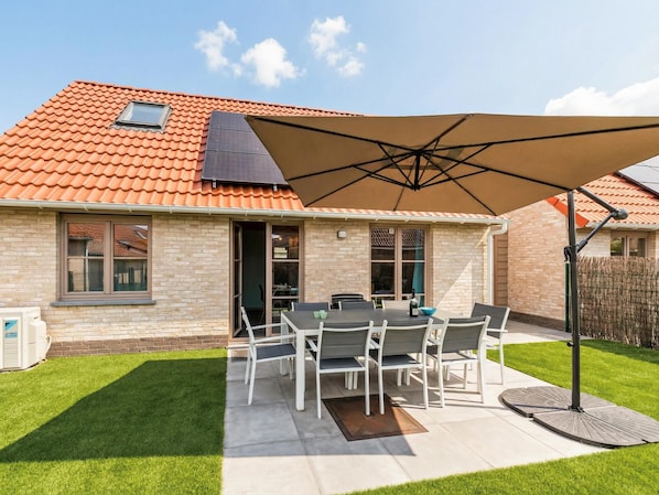A patio with a table and chairs, a large umbrella, and a house with a tiled roof.