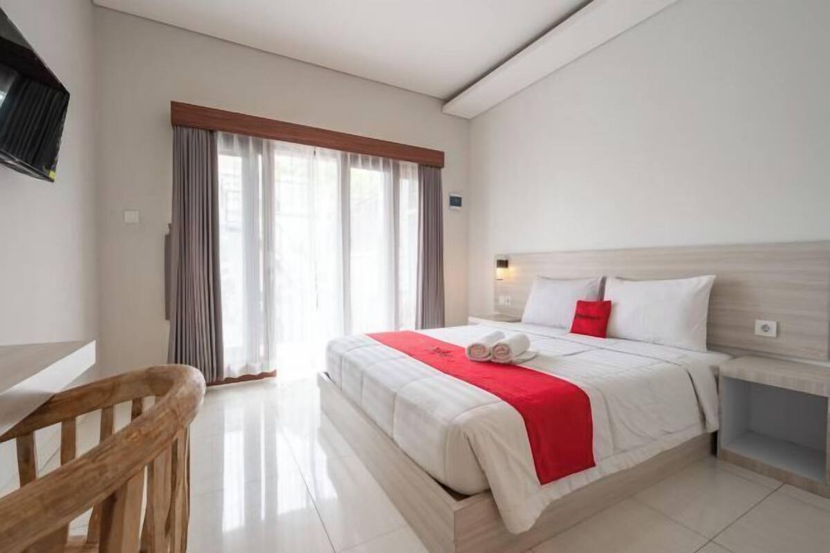 Een hotelkamer met een bed, een houten stoel, een bureau en een raam met gordijnen.