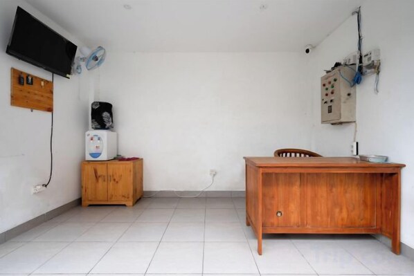 A room with a wooden desk, a television mounted on the wall, and a small cabinet. - RedDoorz Plus @ Yasa’s Living Denpasar (Bali)