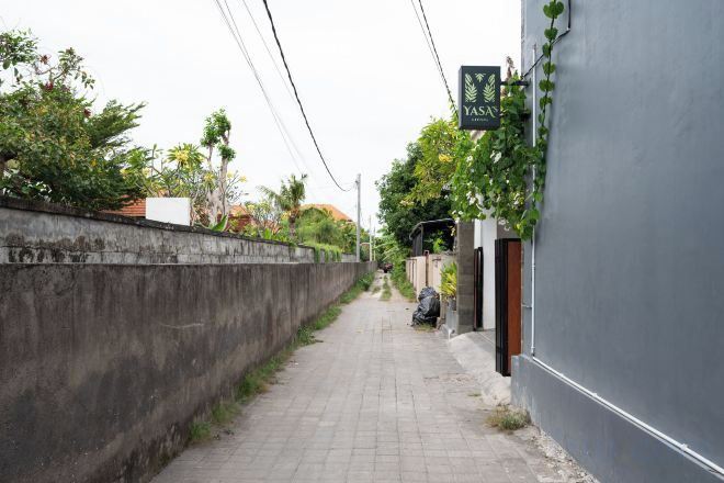 Un callejón estrecho con un muro de concreto a un lado y un edificio con un letrero al otro.