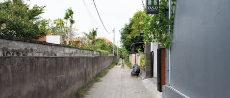 Un callejón estrecho con un muro de concreto a un lado y un edificio con un letrero al otro.